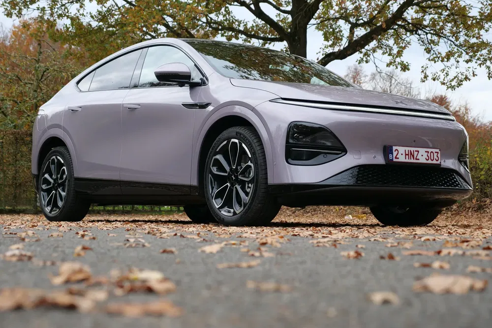 Voiture électrique moderne sur route automnale, plaques d'immatriculation belges, design aérodynamique distinctif.