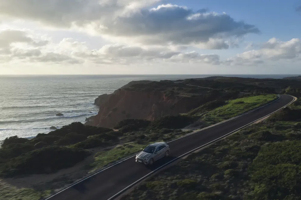 Voiture Mercedes-Benz sur route côtière sinueuse avec vue sur l'océan au coucher de soleil.
