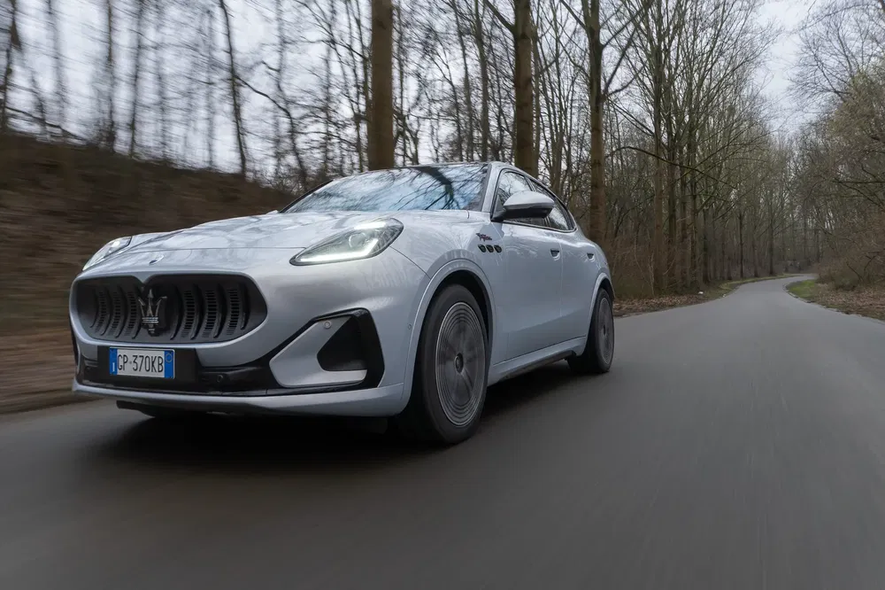 Maserati Grecale argent roulant sur route de campagne bordée d'arbres.
