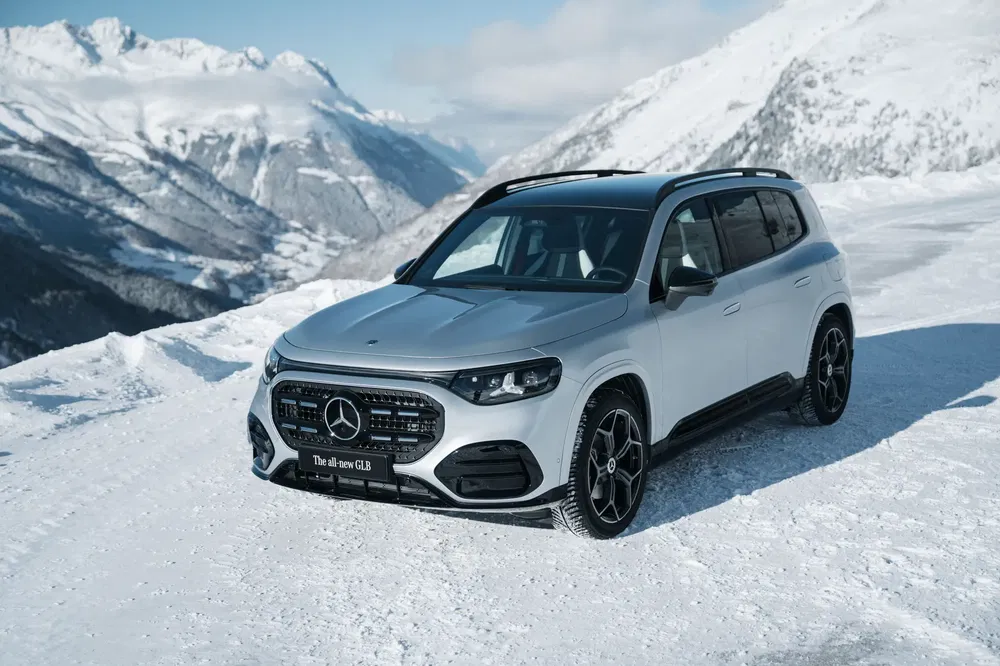 Mercedes-Benz GLB argenté sur neige avec montagnes en arrière-plan par temps ensoleillé.