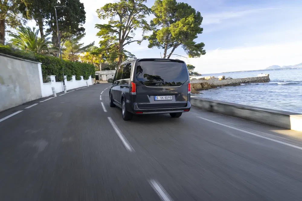 Mercedes T-Klasse bestelwagen rijdt op kustweg omgeven door palmbomen en zee.