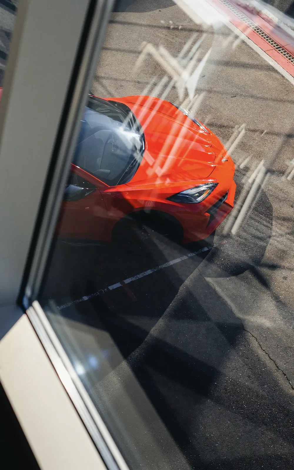 Reflectie van rode Chevrolet Corvette op het circuit, gezien door een raam.