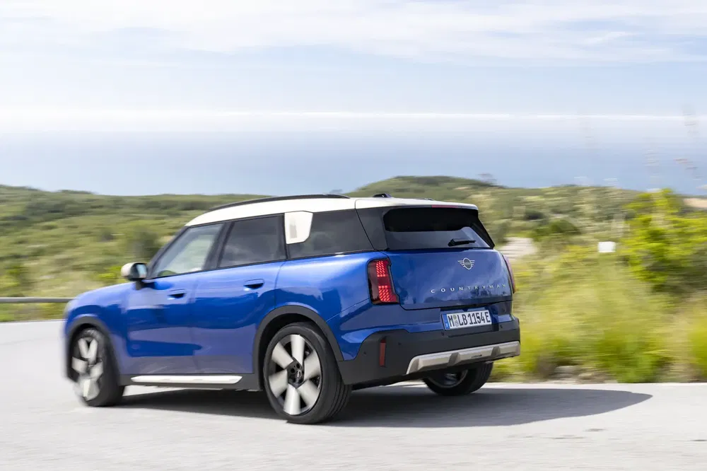 Mini Countryman bleu sur route côtière, arrière plan naturel verdoyant.