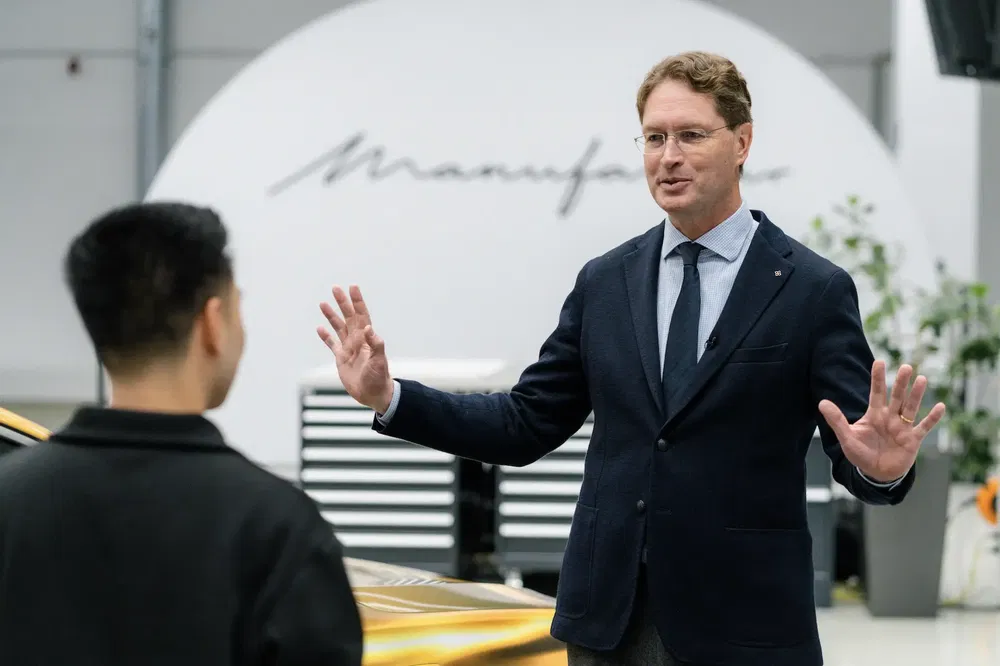 Deux hommes discutant dans un showroom Mercedes, logo visible en arrière-plan.