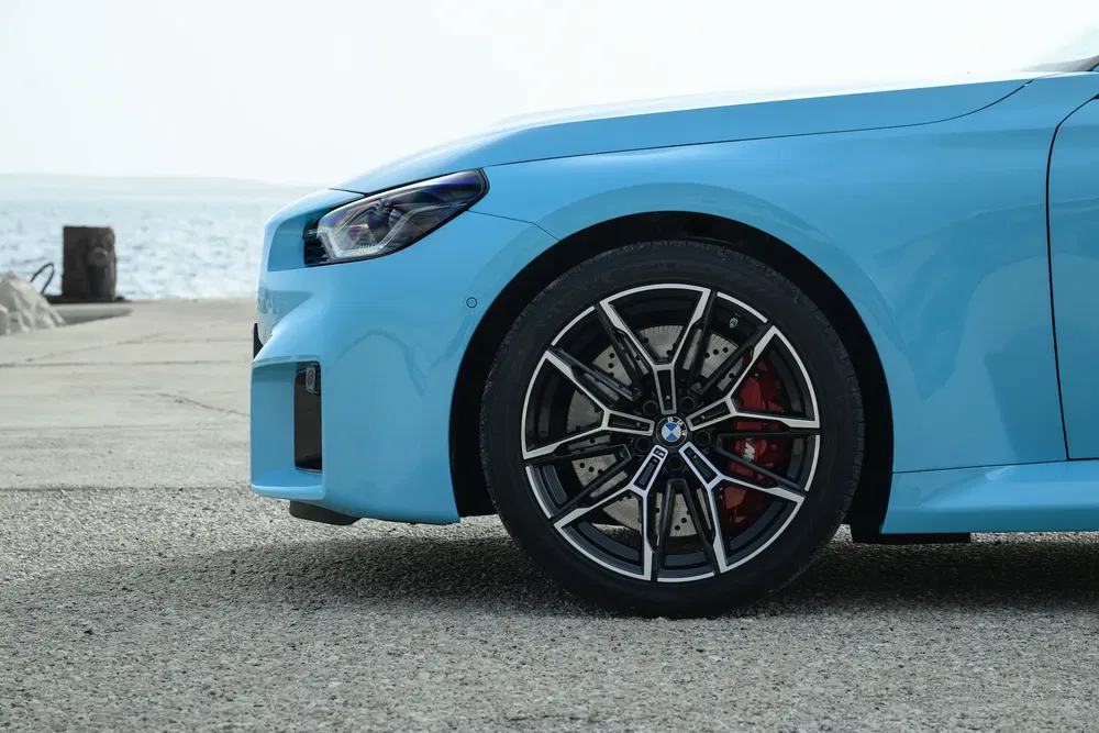 {"fr":"Détail de la roue avant d'une BMW bleue, stationnée près de l'eau.","nl":"Detail van het voorwiel van een blauwe BMW, geparkeerd bij het water."}