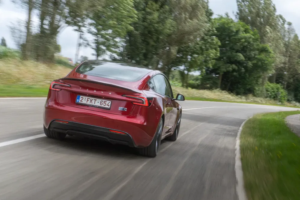Rode Tesla versnelt op slingerende weg omringd door groene bomen.