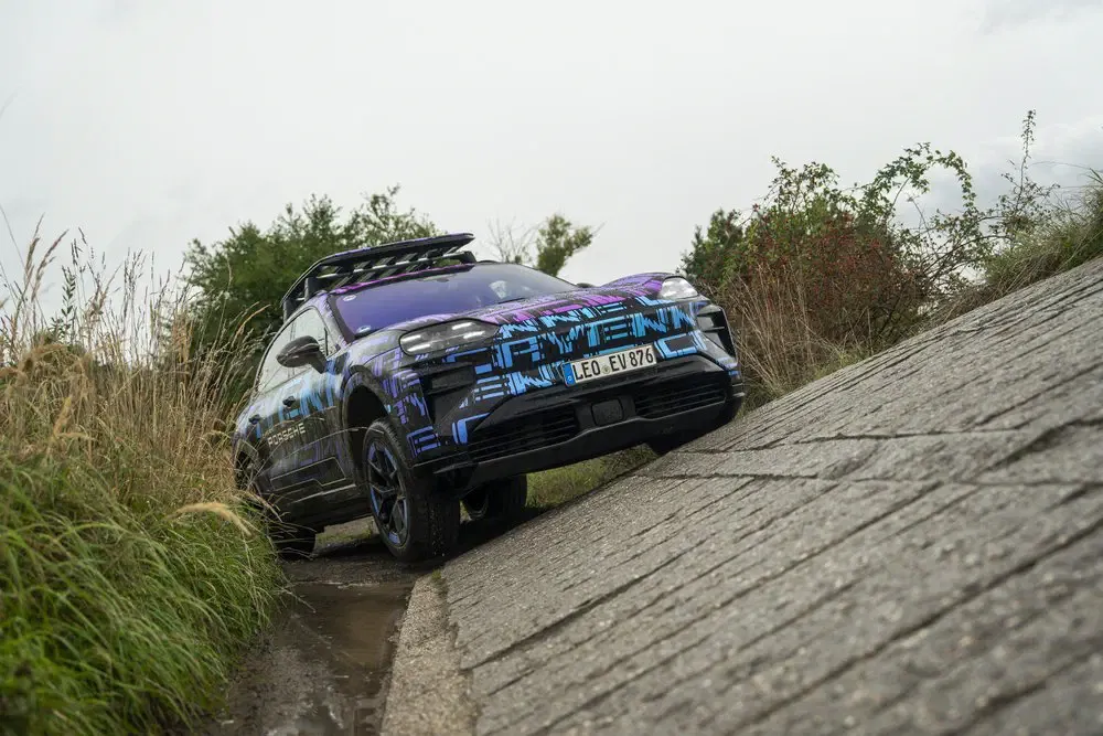 Elektrische Porsche Macan SUV op off-road parcours met futuristische blauw-zwarte camouflage.