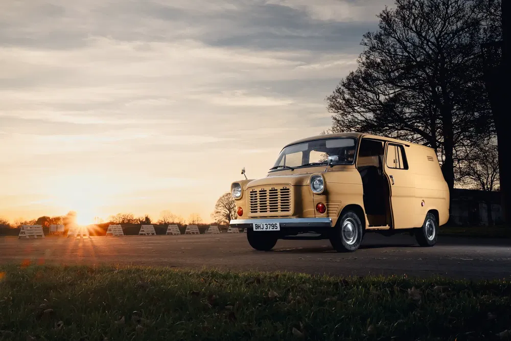Fourgon Ford Transit classique jaune au coucher du soleil sur une route déserte.