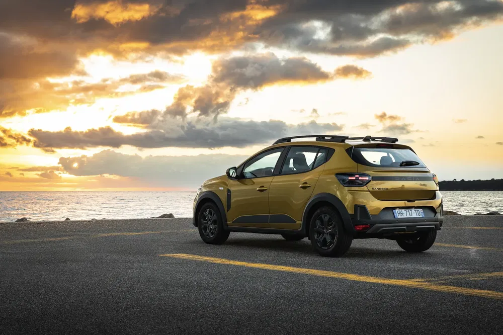Dacia Sandero Stepway jaune au coucher de soleil près de la mer.