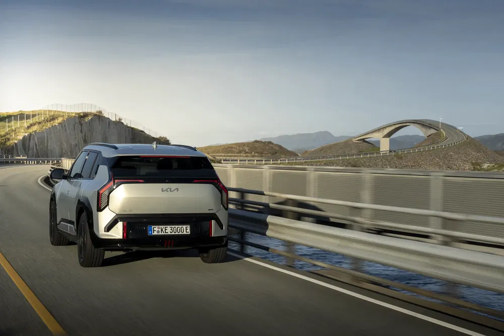 Kia EV9 roulant sur une route panoramique avec un pont en arrière-plan.
