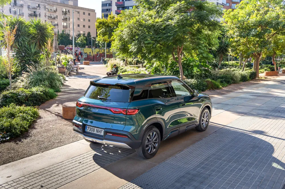 SUV vert BYD Atto 3 garé dans un espace urbain arboré et moderne.