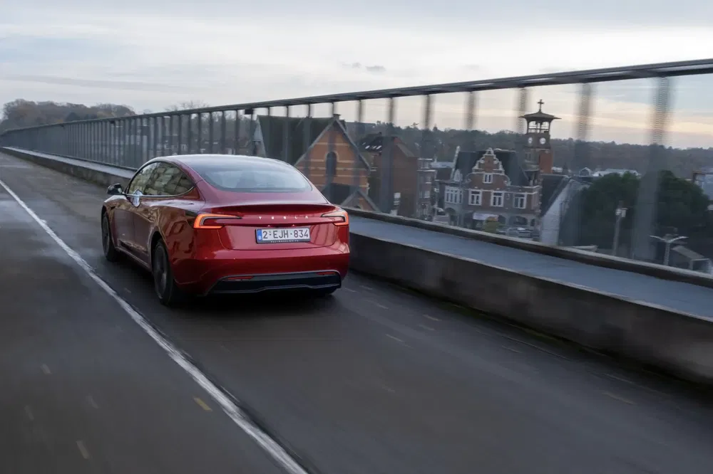 Rode Tesla Model S rijdt over brug met uitzicht op stad.
