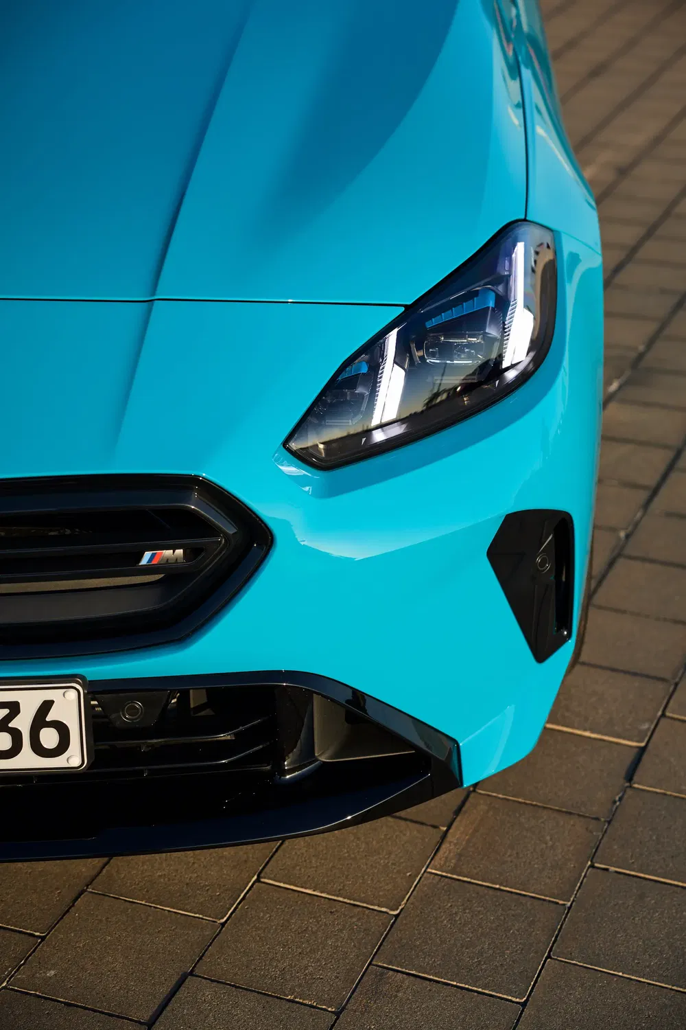 Vue avant d'une BMW M2 bleue avec phare distinctif et plaque partiellement visible.