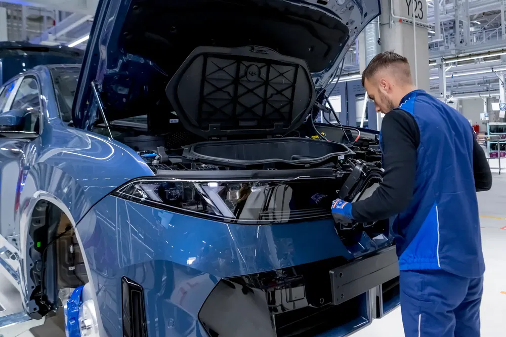 Technicus werkt aan elektrische BMW iX SUV in een moderne fabriekshal.