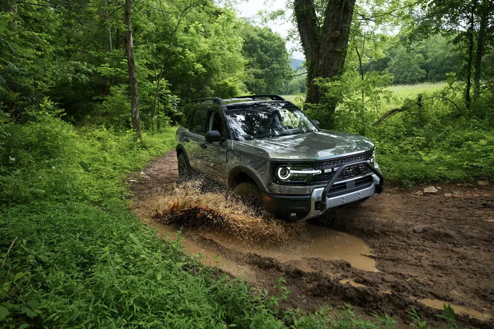 Ford Bronco Sport traversant des chemins boueux en forêt verdoyante.