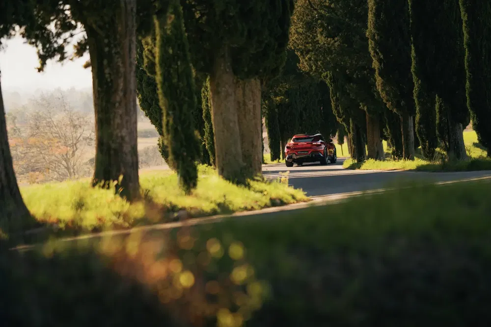 Voiture rouge roulant sur une route bordée d'arbres, ambiance automnale sereine.