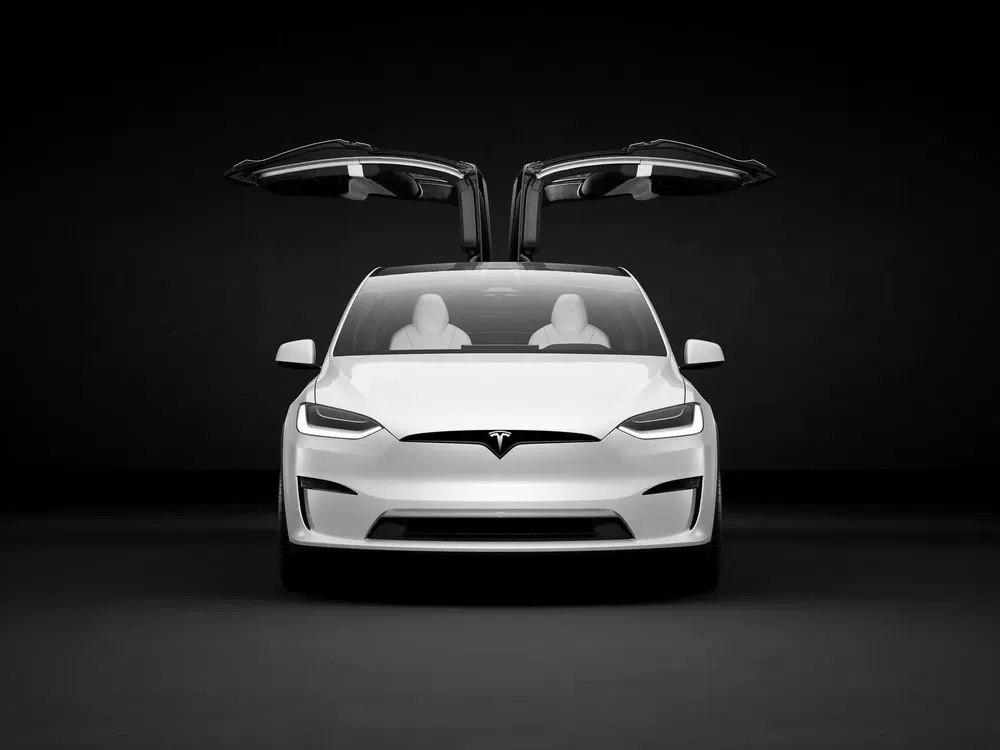 Tesla Model X blanche avec portes papillon ouvertes, vue de face sur fond noir.