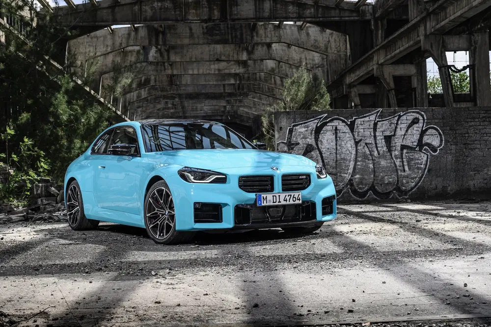BMW M2 bleu clair dans un bâtiment abandonné avec graffiti.