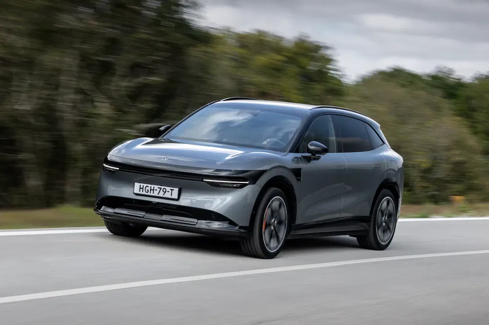 Voiture électrique XPeng G9 grise roulant sur une route, arbres flous en arrière-plan.