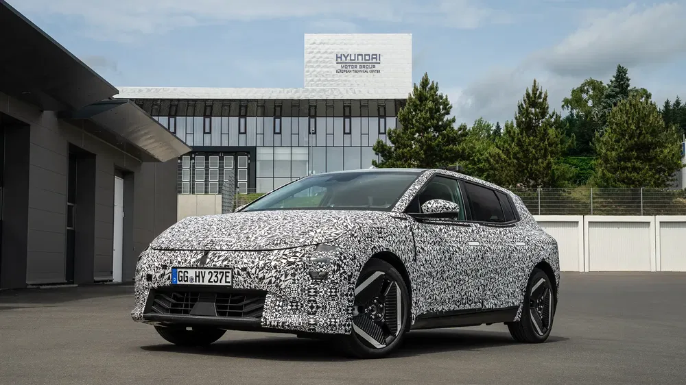 Voiture camouflage Hyundai devant centre de recherche, design électrique futuriste en extérieur.