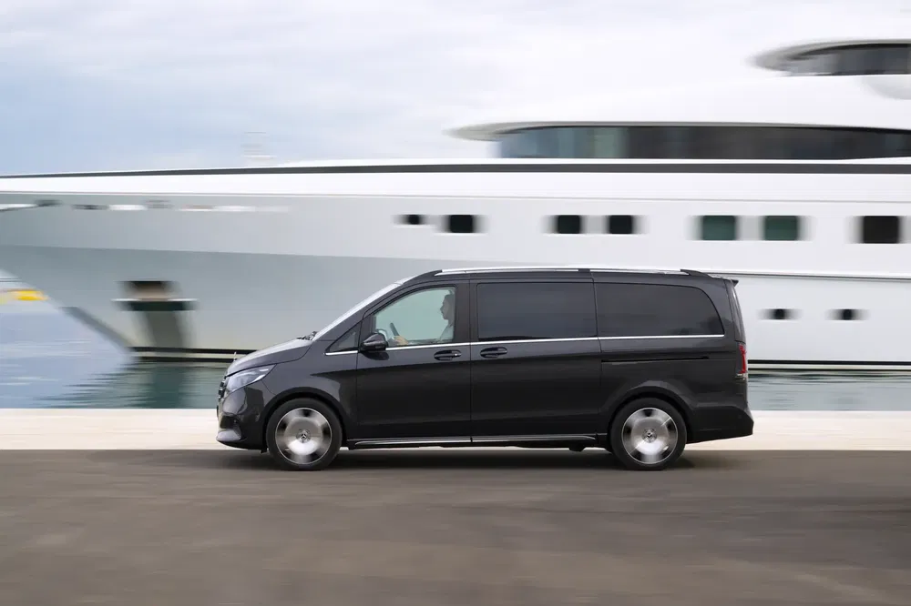 Zwarte Mercedes-Benz V-Klasse rijdend langs een luxe jacht op de achtergrond.