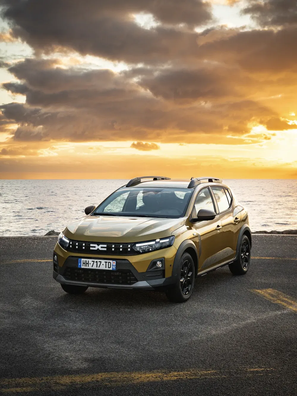 Dacia Sandero Stepway dorée au bord de la mer, au coucher du soleil spectaculaire.