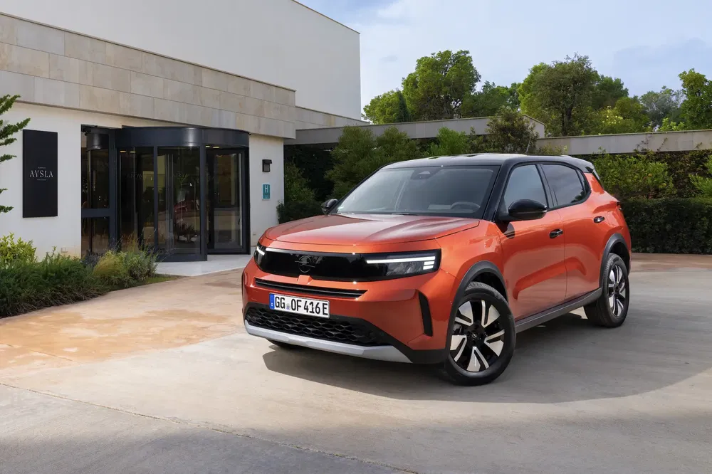 SUV Opel Mokka électrique orange garé devant un bâtiment moderne.
