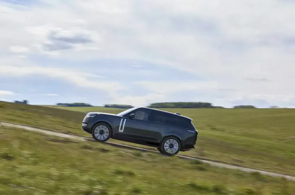 SUV Range Rover moderne roulant à travers une campagne vallonnée sous un ciel nuageux.