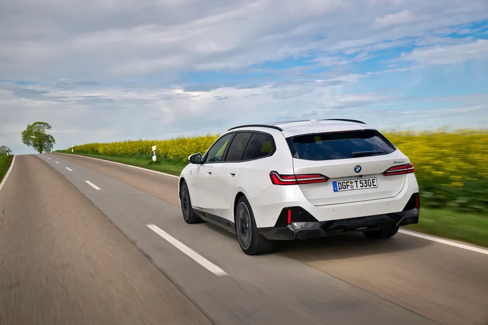 BMW i5 Touring électrique sur route de campagne, ciel partiellement nuageux.