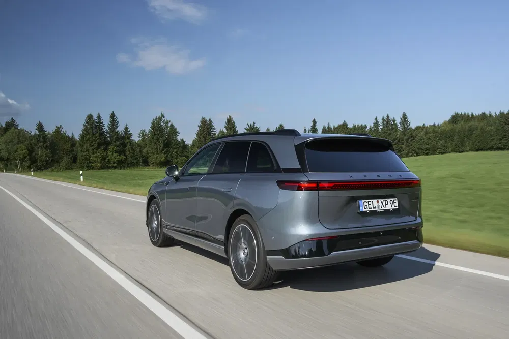 Elektrische auto Zeekr 001 rijdt op een weg omgeven door bomen, slanke moderne vormgeving.