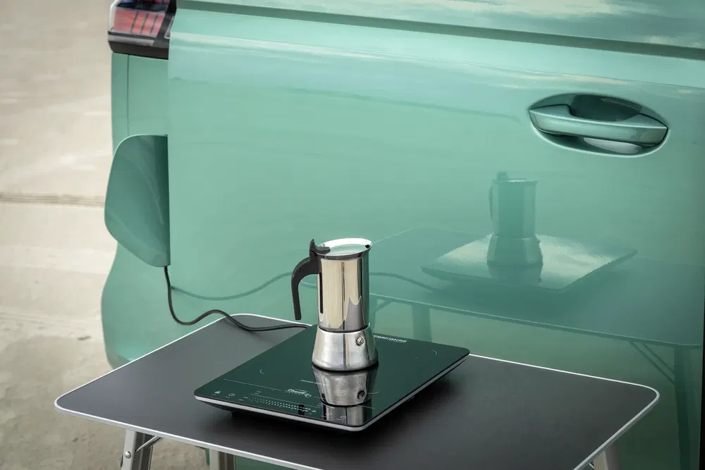 Voiture électrique verte avec cafetière connectée à une prise extérieure sur une plaque à induction.