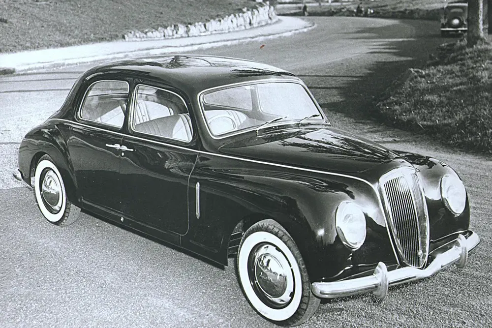 Voiture classique Lancia avec pneus à flancs blancs sur une route sinueuse.