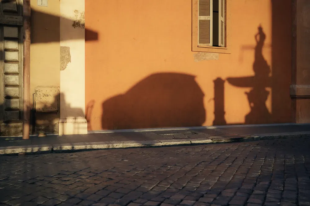{"fr":"Ombre de voiture sur mur orange avec fontaine et fenêtre, rue pavée ensoleillée.","nl":"Schaduw van auto op oranje muur met fontein en raam, zonnige kasseienstraat."}