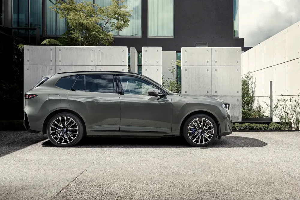 BMW iX1 gris stationné devant une maison moderne avec murs de béton.