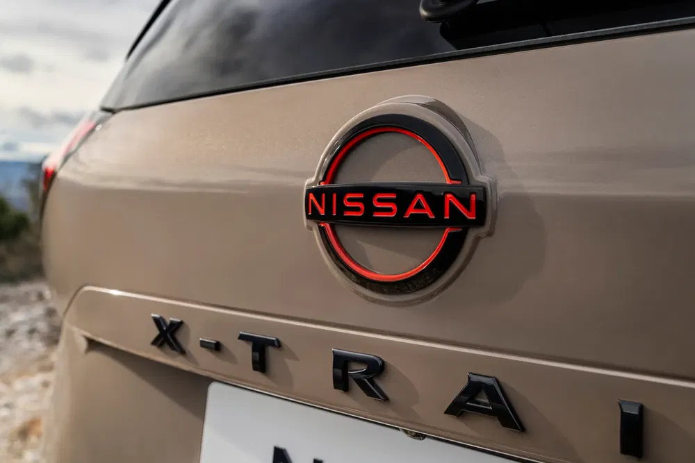 Achterembleem van een beige Nissan X-Trail met opvallend rood logo.