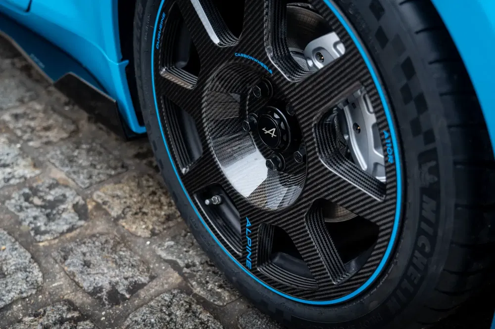 Alpine carbonvelg met Michelin-band op klinkers, sportief blauw-zwart ontwerp.