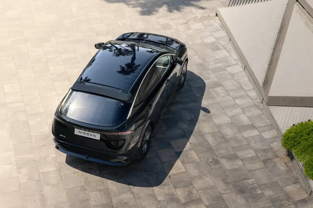 Luchtfoto van een zwarte Nissan Ariya op een betegelde oprit met boomschaduwen.