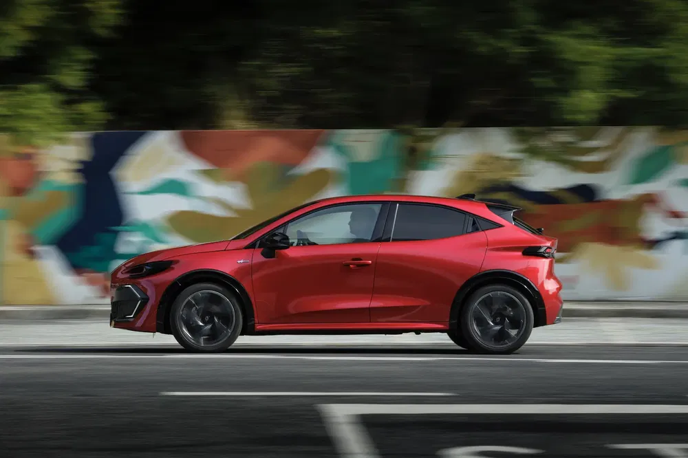 Voiture électrique rouge, profil latéral, devant mur coloré, conduite en ville.