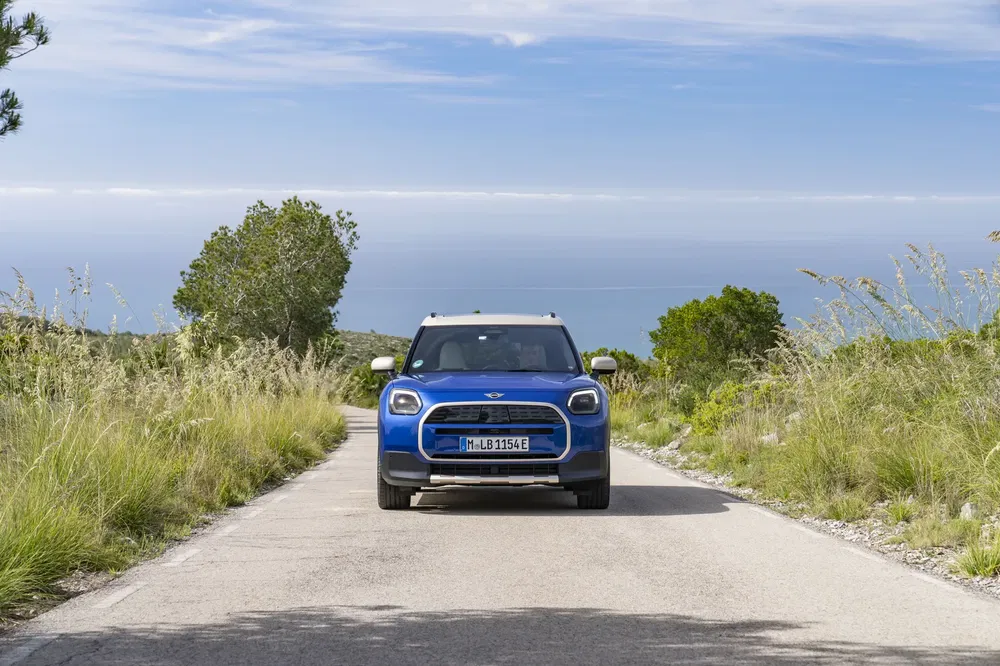 Mini Countryman bleu sur une route de campagne avec vue sur la mer.