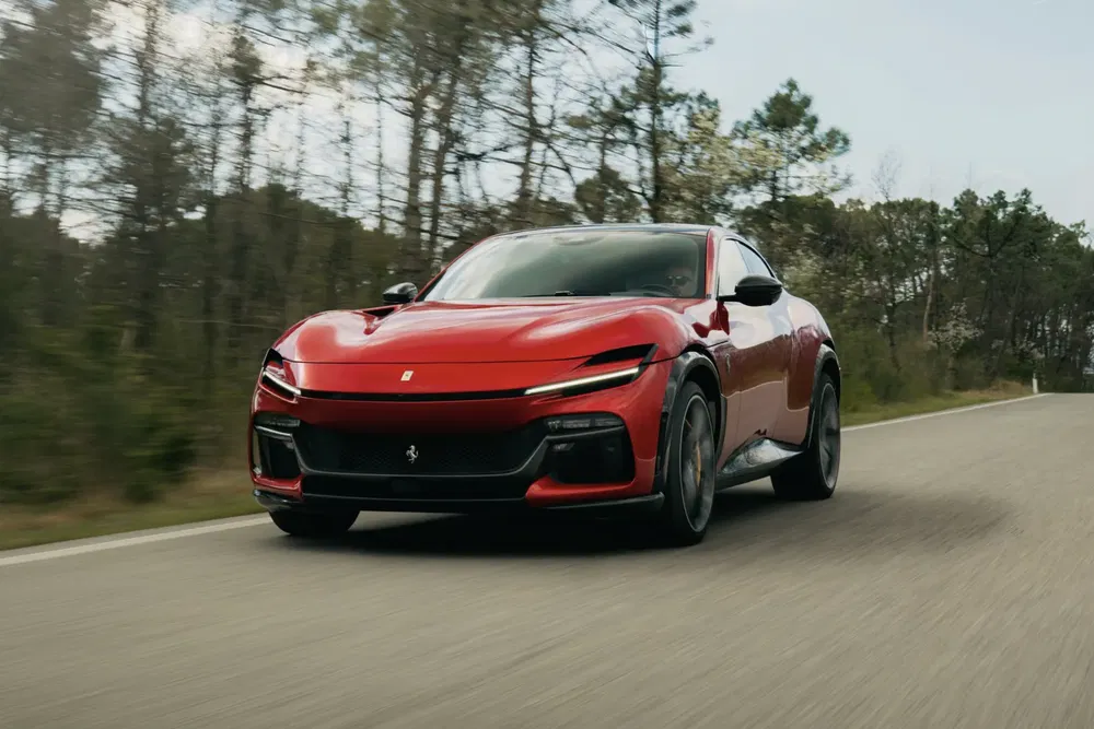 Ferrari Purosangue rouge roulant sur une route bordée d'arbres.