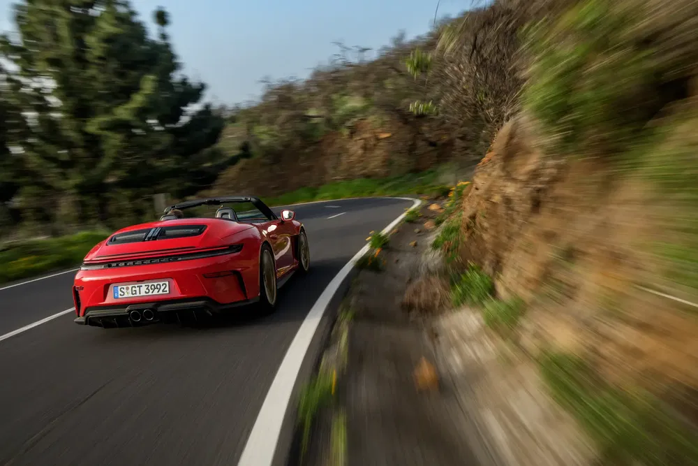 Porsche 911 cabriolet rouge accélérant sur une route sinueuse de montagne verdoyante.