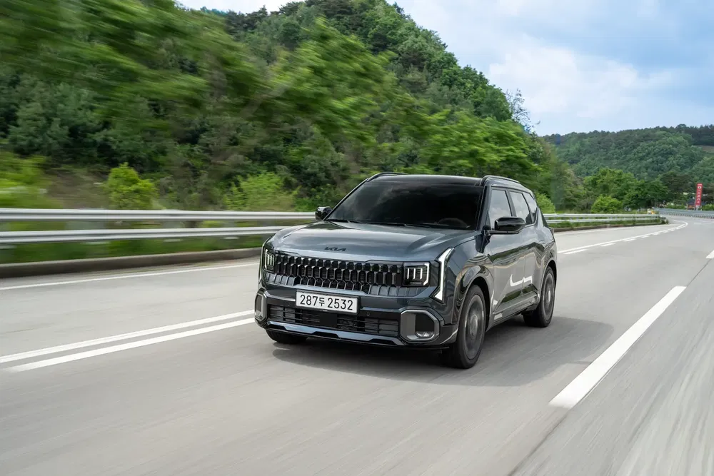 SUV Kia roulant sur une autoroute bordée d'arbres, ciel bleu en arrière-plan.