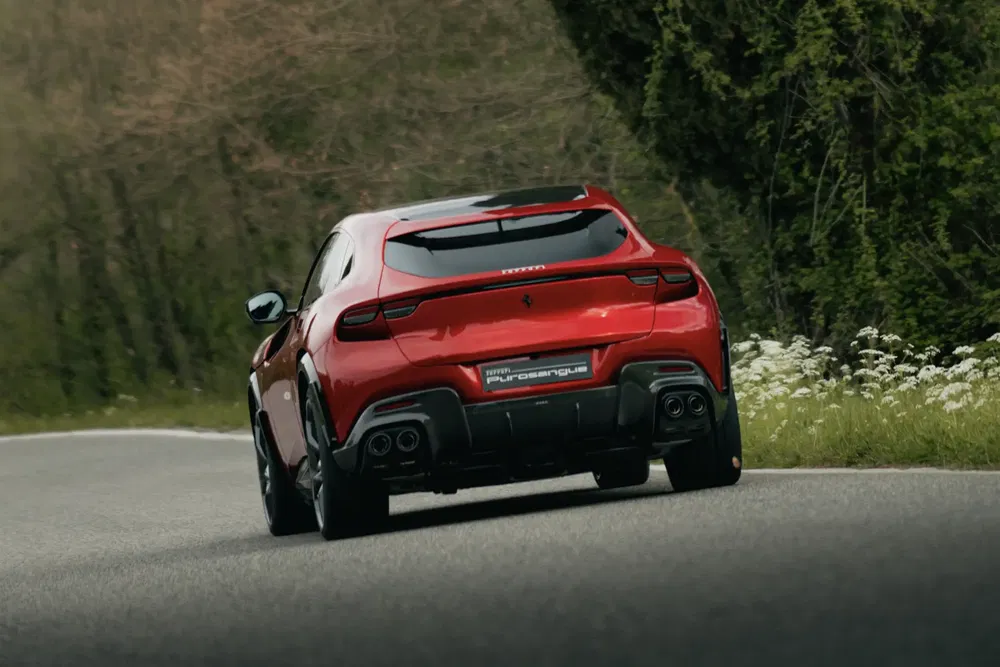 Ferrari Purosangue rouge, vue arrière sur route sinueuse bordée d'arbres.