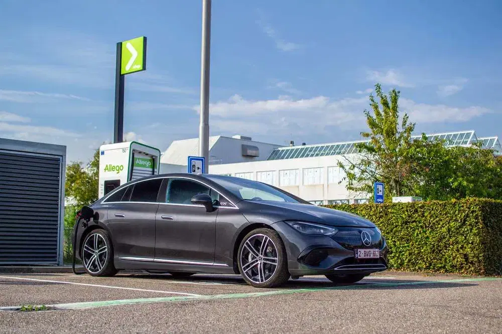 Zwarte Mercedes EQS bij Allego oplaadstation onder een heldere lucht.
