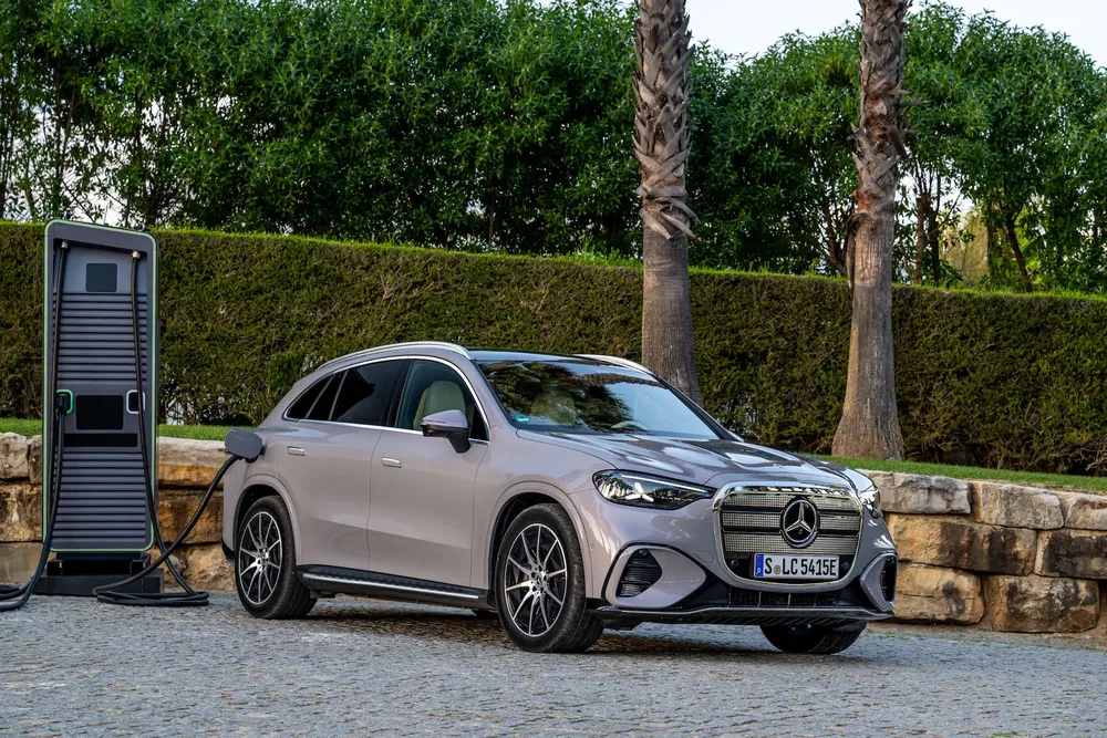 Mercedes électrique en charge sur une borne, entourée de palmiers et de verdure luxuriante.