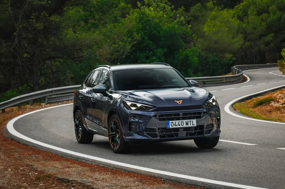 Zwarte Cupra SUV op kronkelige weg omringd door weelderig bos.