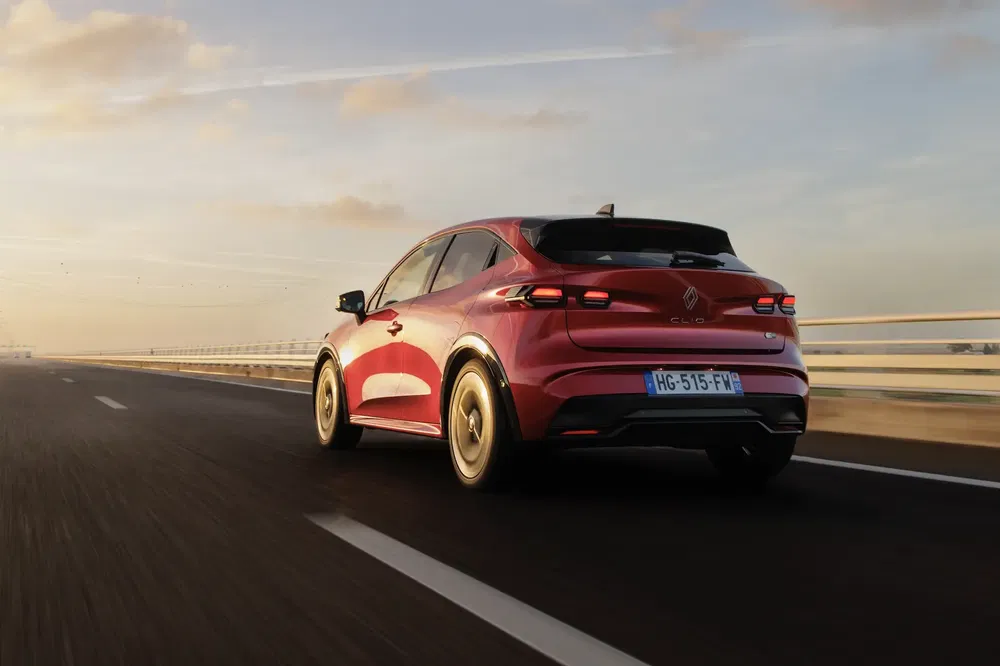 Renault Clio rouge roulant sur l'autoroute au coucher du soleil, vue de l'arrière.