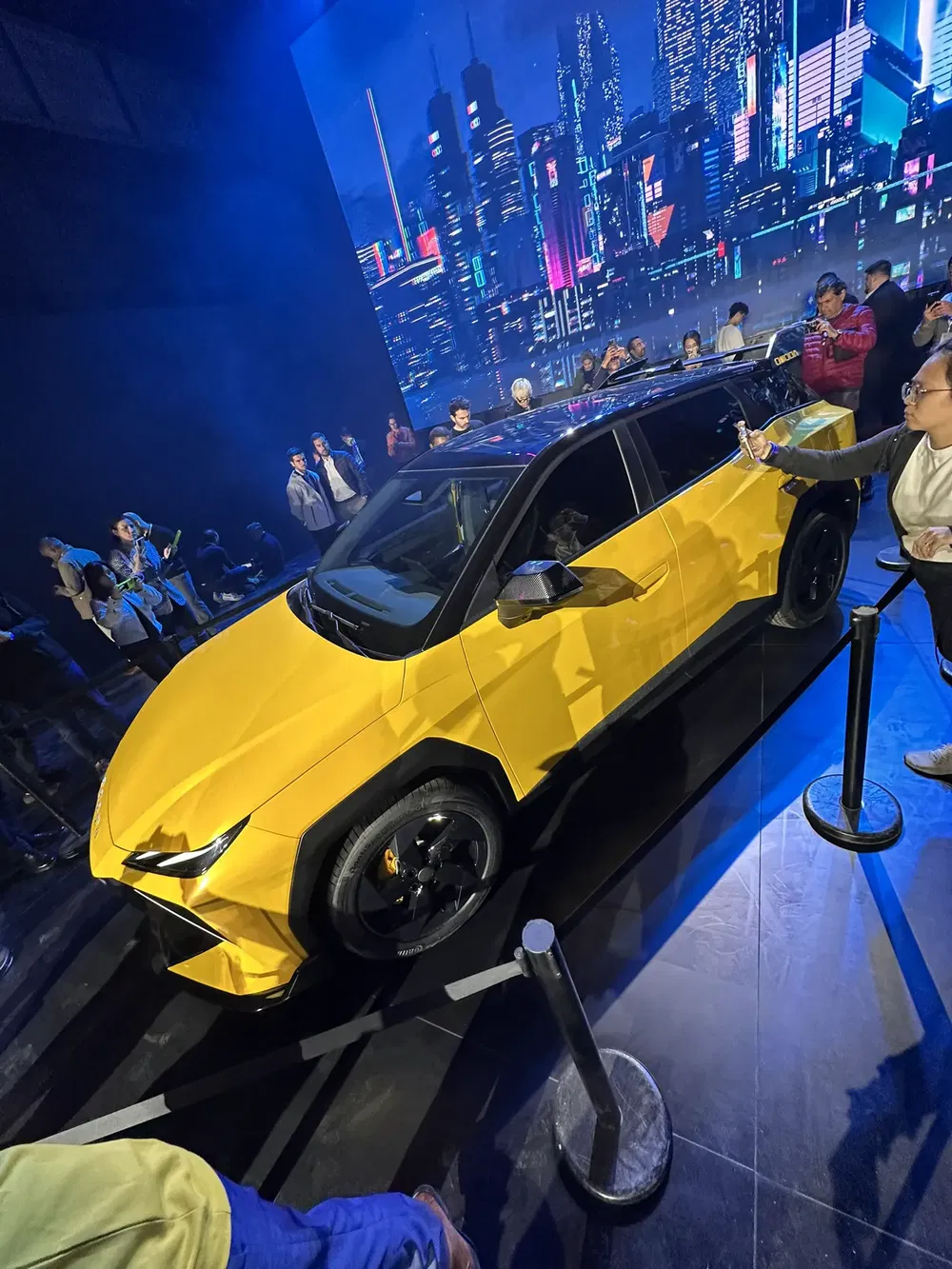 Nouvelle voiture électrique jaune exposée avec un fond urbain moderne en arrière-plan.