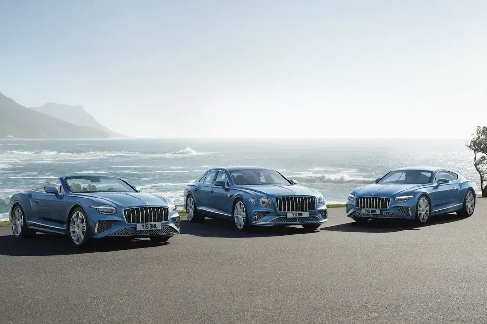 Collection de voitures Bentley bleues alignées sur une route côtière panoramique.