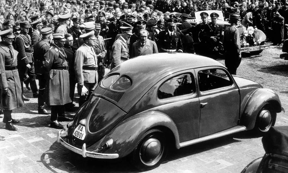 Volkswagen Coccinelle historique entourée de militaires en uniforme pendant un rassemblement.